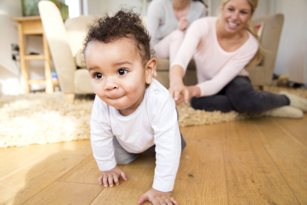 mother who wanted to adopt a child smiles as the child crawls across the floor